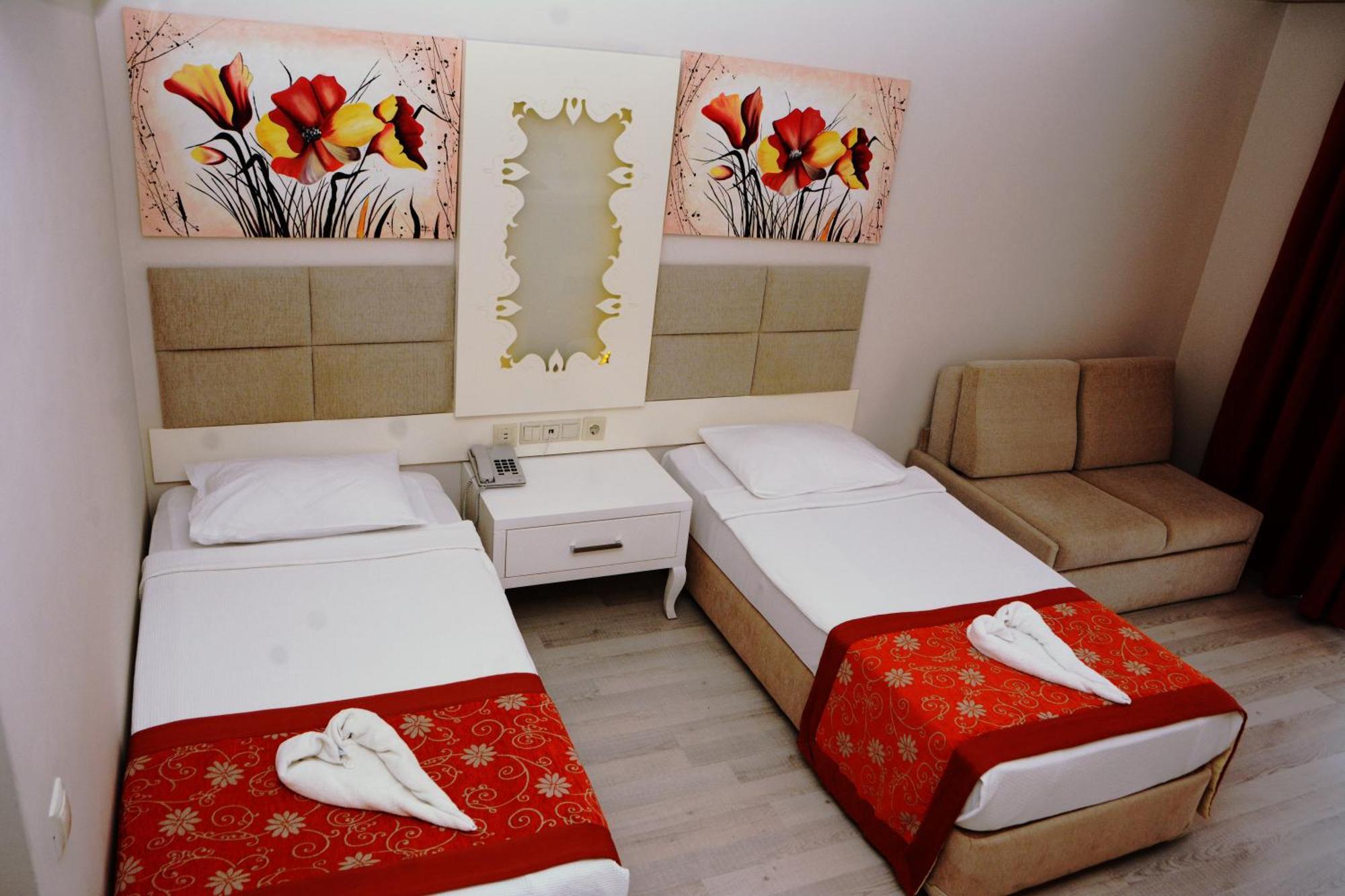 Miramor Hotel & Spa Antalya Exteriör bild The photo shows a hotel room featuring two single beds with white linens, each adorned with a decorative red throw. The headboards are upholstered in a light beige fabric. Above the beds, there are two large artwork pieces depicting colorful flowers.