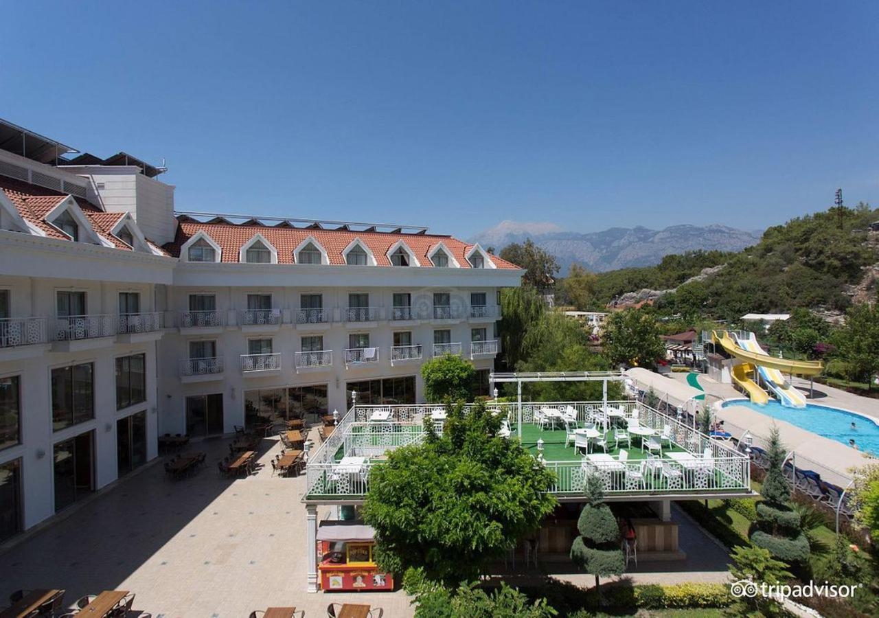 Miramor Hotel & Spa Antalya Exteriör bild The photo shows a hotel or resort facility with a well-maintained exterior. There is a large green area with grass and some trees, likely intended for relaxation or recreational activities. In the background, there are water slides suggesting an amus